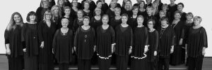 A black and white photo of a choir of women, posing for a group photo.